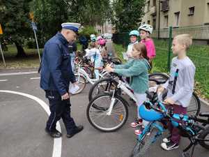 Zdjęcie przedstawia policjanta ruchu drogowego sprawdzającego stan techniczny roweru wraz z uczniami