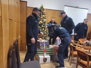 Zdjęcie przedstawia policjantów i strażników miejskich układających prezenty pod choinką