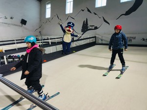 Zdjęcie przedstawia dzieci na sztucznym stoku narciarskim, w tle Sznupek